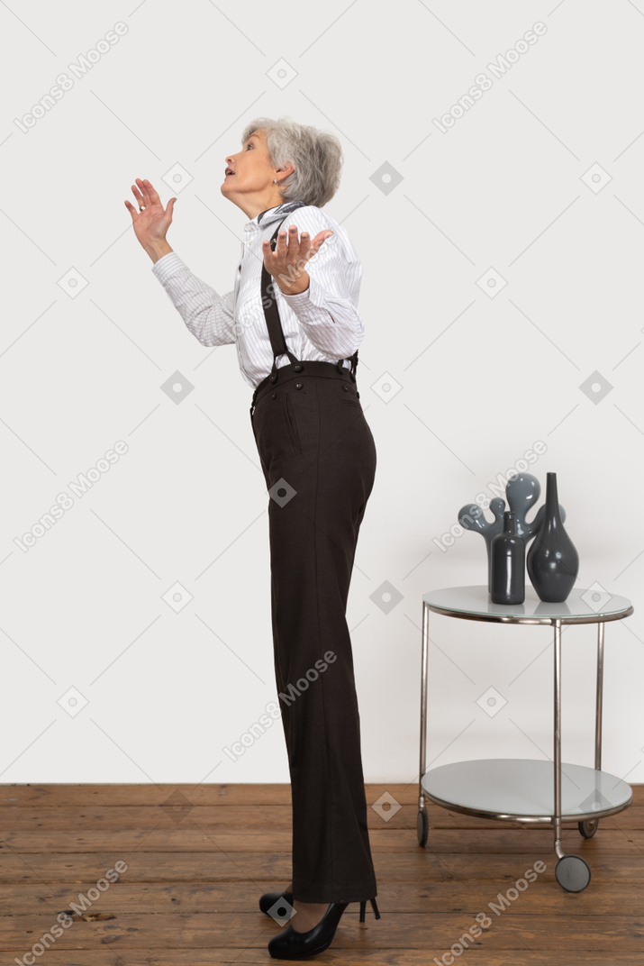 Side view of an old lady in office clothing raising hands while looking for something