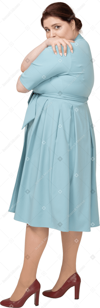 Side view of a woman in blue dress hugging herself