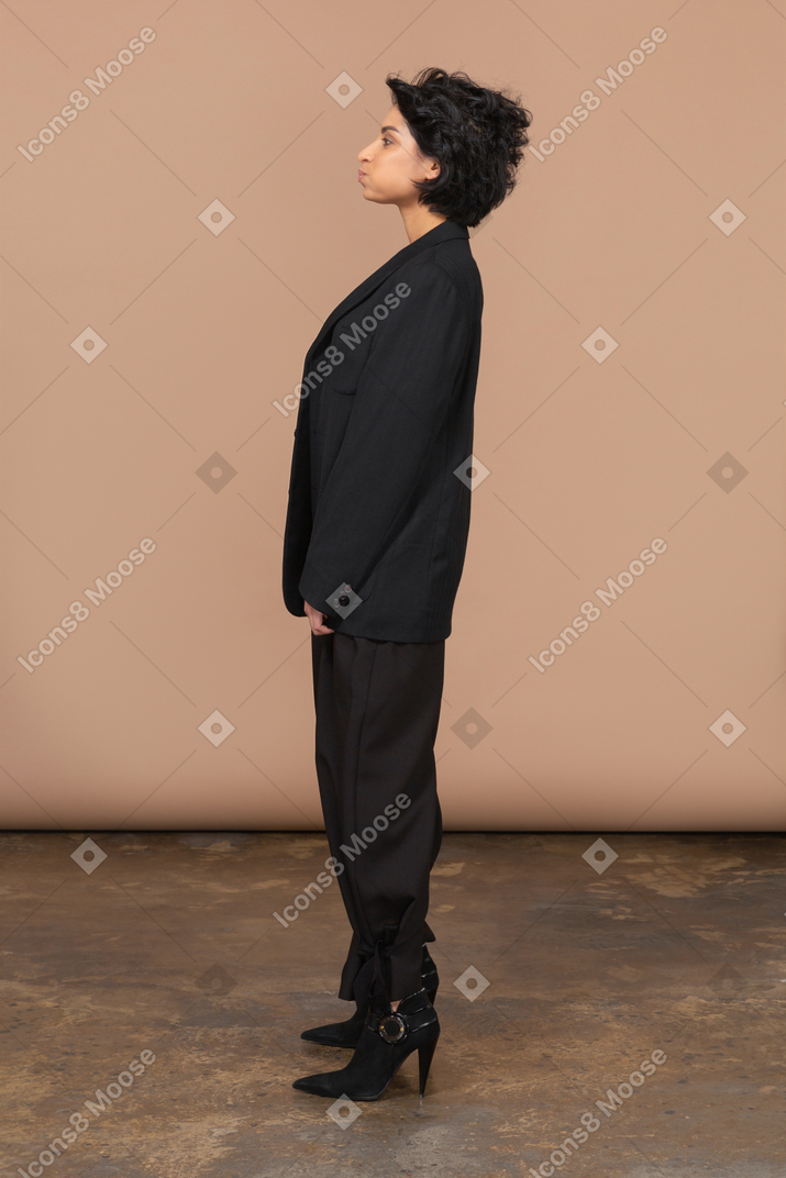 Вид сбоку деловой женщины в черном костюме, надувающейся и смотрящей в сторону