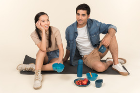 Interracial couple sitting on karimat near dishes