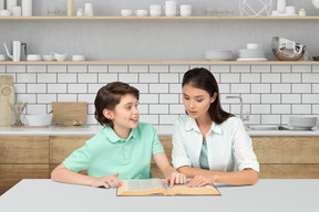 A woman and a boy reading a book in a kitchen