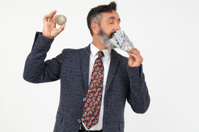 Hombre maduro que huele billetes de dólar y sosteniendo un bitcoin