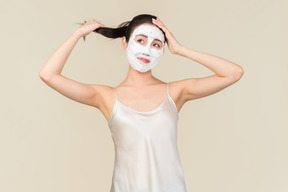 Rêveuse jeune femme asiatique avec masque facial touchant les cheveux