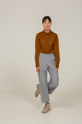 Vista frontal de uma jovem mulher asiática de calça e blusa cruzando as pernas