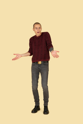 Front view of a young surprised man in red pullover outspreading his hands