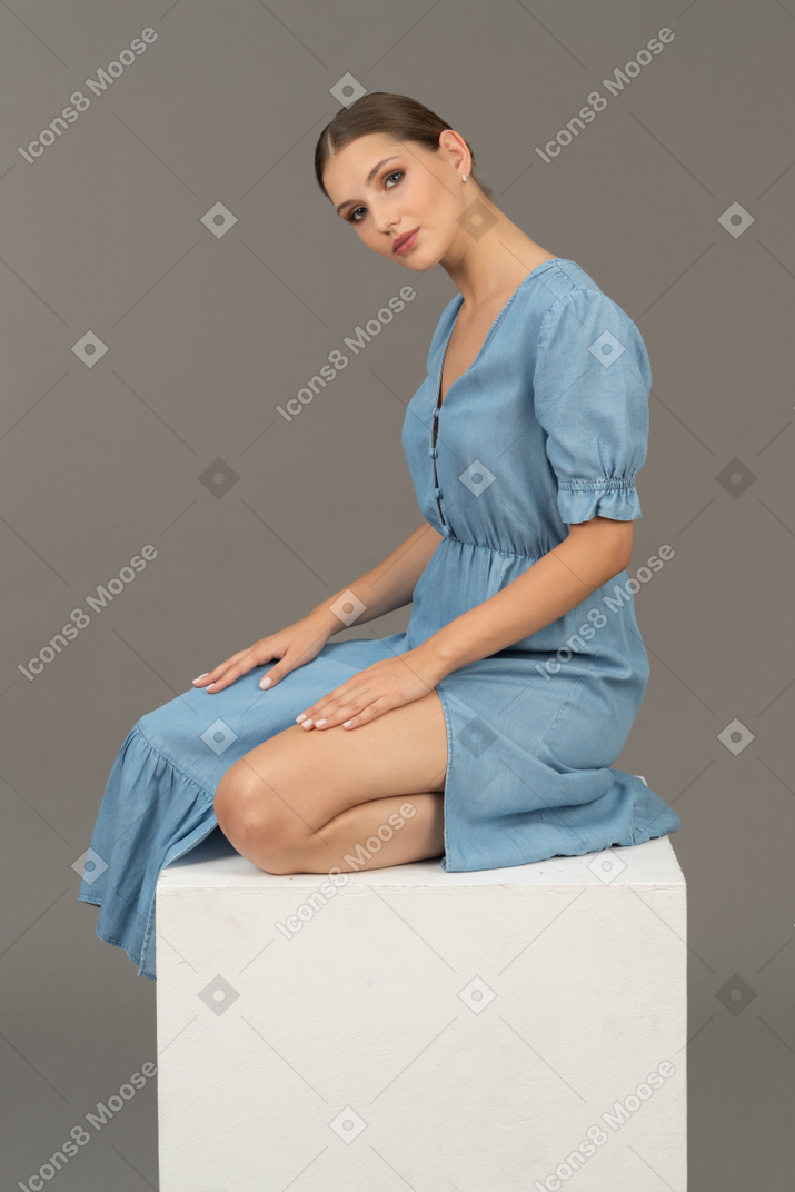 Vista lateral de uma jovem de vestido azul, sentado em um cubo