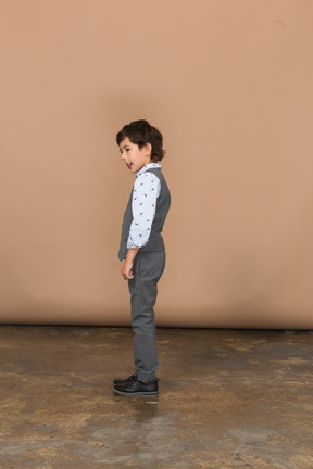 Vista lateral de um lindo garoto de terno cinza mostrando a língua