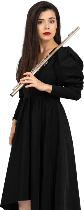 Vista di tre quarti di una giovane donna seria in vestito nero che tiene flauto