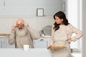 Hombre de edad cerrando los ojos con galletas y una mujer joven que lo mira