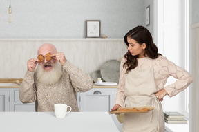 Aged man closing eyes with cookies and young woman looking at it