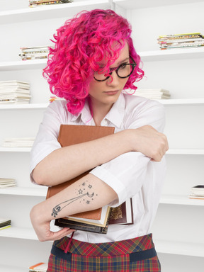 A woman with pink hair and glasses holding books