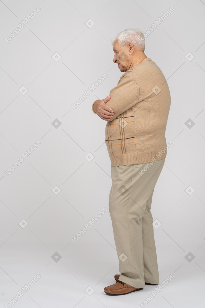一位身穿休闲服、双臂交叉站立的老人的侧视图