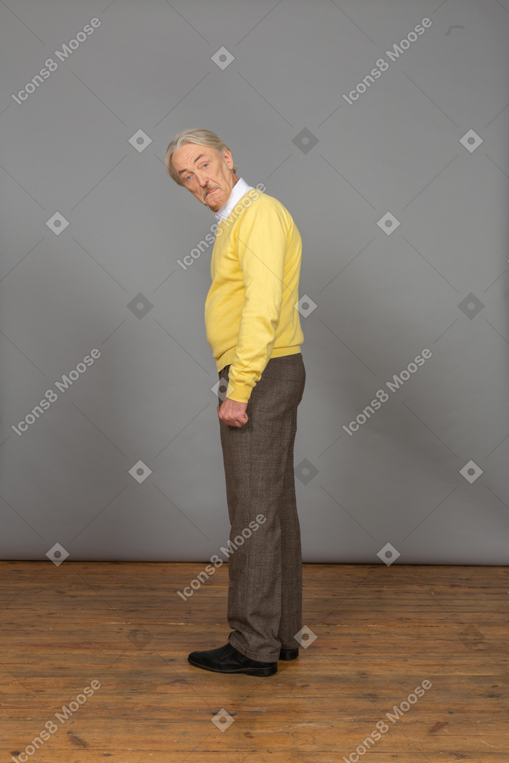 노란색 스웨터 아래로 구부리고 카메라를보고 놀란 노인의 측면보기