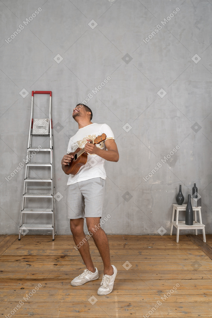 Вид в три четверти на мужчину, играющего на укулеле и счастливо откидывающегося назад