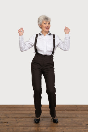 Front view of a happy old lady in office clothing raising hands