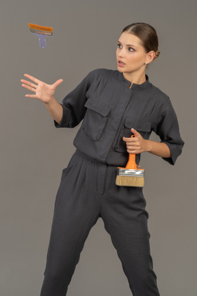 Woman in gray coveralls tossing a paint brush into the air