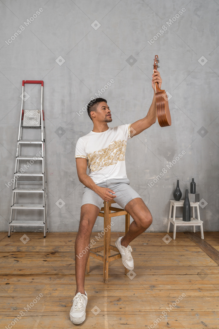 Front view of a man on a stool holding up a ukulele