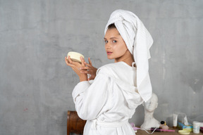 Vista traseira de uma mulher de roupão aplicando creme para as mãos