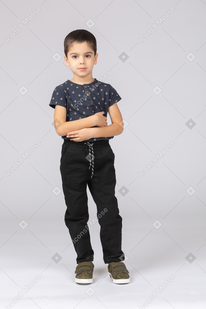 Vista frontal de um lindo menino em pé com os braços cruzados e olhando para a câmera