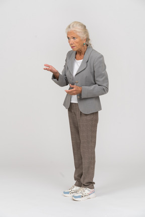 Vista laterale di una signora anziana seria in abito che spiega qualcosa