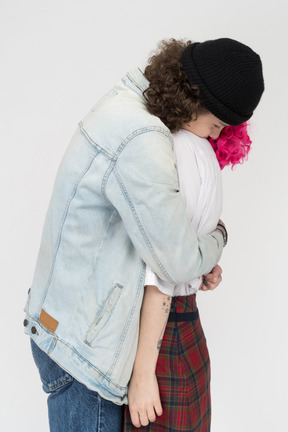 Side view of a teen male in a denim shirt hugging his girlfriend