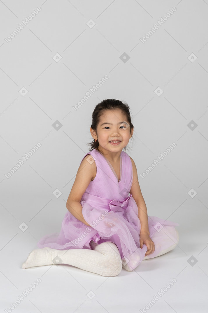 Ragazza in un vestito rosa seduto sul pavimento e guardando la fotocamera