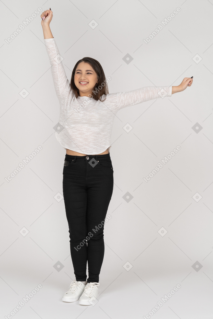 Front view of a smiling young dancing indian female in casual clothes raising hands