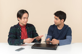 Deux jeunes geeks assis à la table et ayant des problèmes pour réparer l'ordinateur portable
