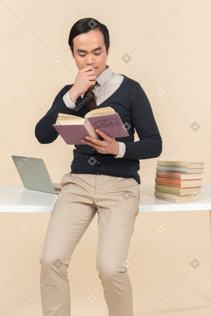 Young asian student biting his finger while reading a book