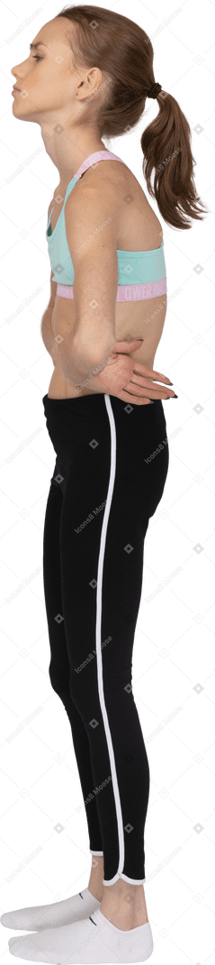 Vista laterale di una ragazza adolescente stanca in abiti sportivi che mette le mani sui fianchi