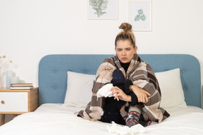 Vista frontal de una joven enferma en pijama envuelto en una manta de cuadros