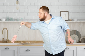 A man holding a duster brush in a kitchen