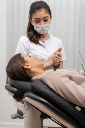 Un dentista femminile che parla con la sua paziente femminile mentre mette insieme le mani