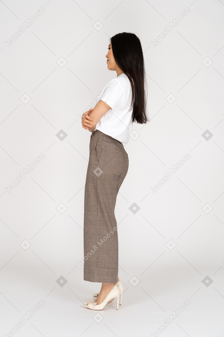 Vista laterale di una giovane donna sospettosa in calzoni e t-shirt attraversando le mani