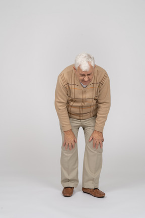 Front view of an old man bending down and touching his hurting knees