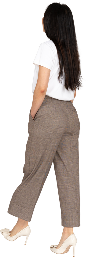 Vista posteriore di tre quarti di una giovane donna che cammina in calzoni e t-shirt mettendo la mano in tasca