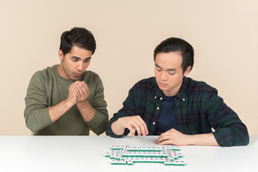 Young interracial friends sitting at the table and playing scramble game
