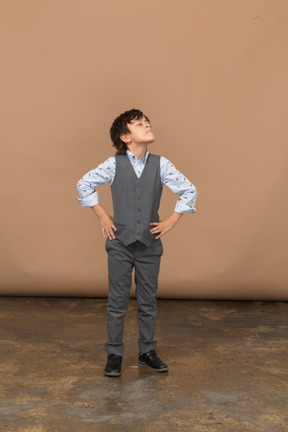 Vista frontal de um menino de terno cinza posando com as mãos nos quadris