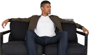 Vista frontal de um jovem sentado em um sofá segurando um cigarro na boca