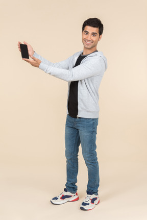 Young caucasian man presenting smartphone