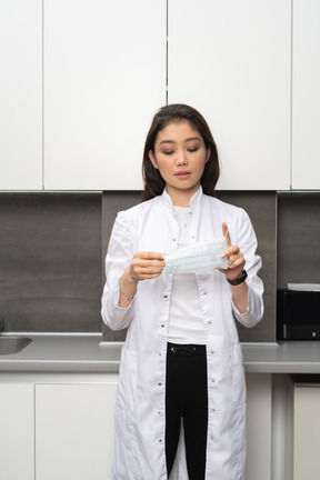 Woman in white lab coat putting on medical mask