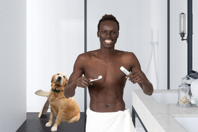 Man brushing his teeth in the bathroom with dog sitting in the background