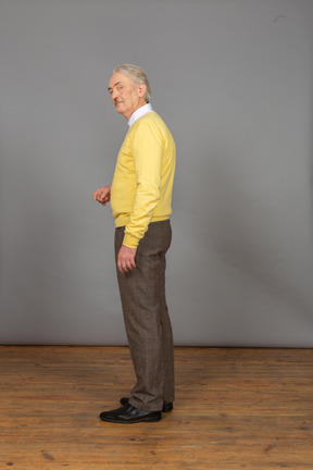 Side view of a thoughtful old man raising hand and looking at camera
