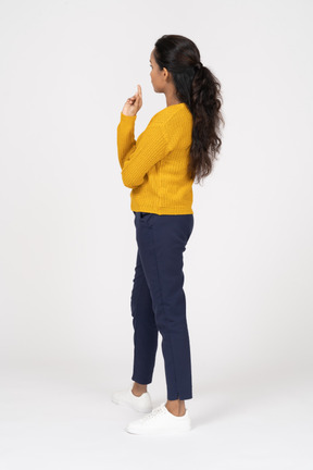 Vista lateral de uma garota pensativa em roupas casuais apontando para cima com um dedo