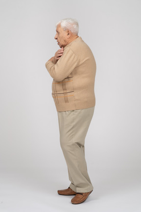 Vista lateral de un anciano asustado con ropa informal de pie con las manos en los hombros