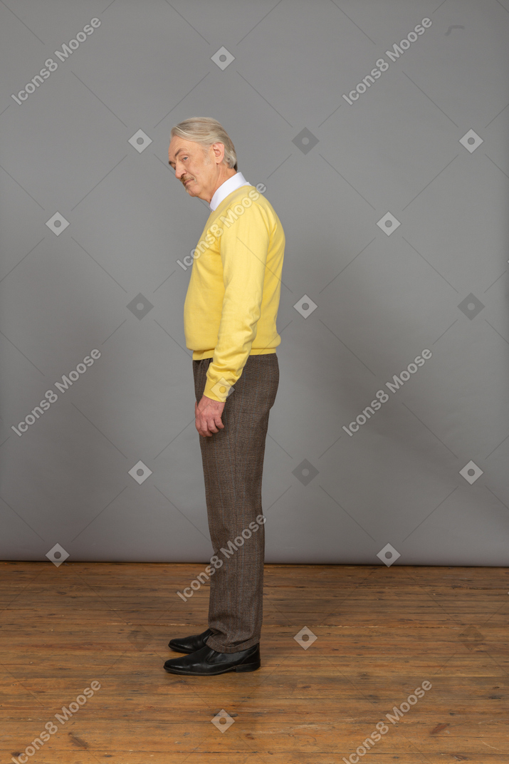 黄色のプルオーバーで前に傾いて脇を見て驚いた老人の側面図