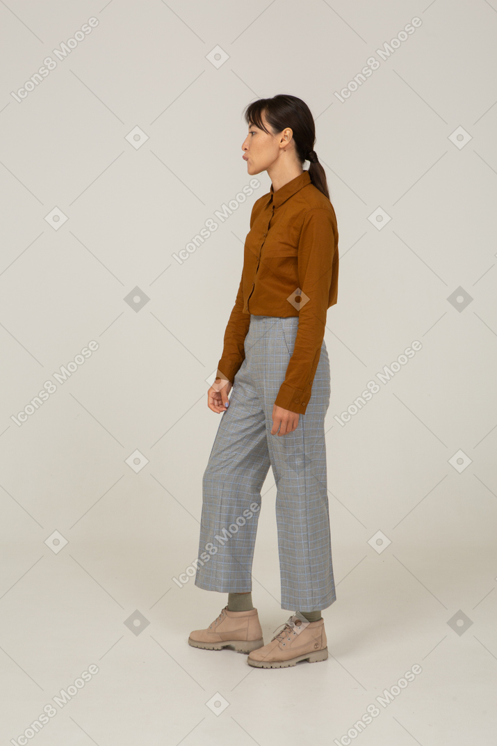Vista lateral de uma jovem mulher asiática de calça e blusa mordendo o lábio