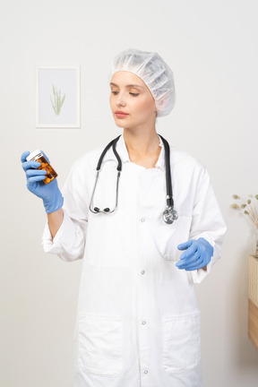 Front view of a young female doctor holding a jar of pills