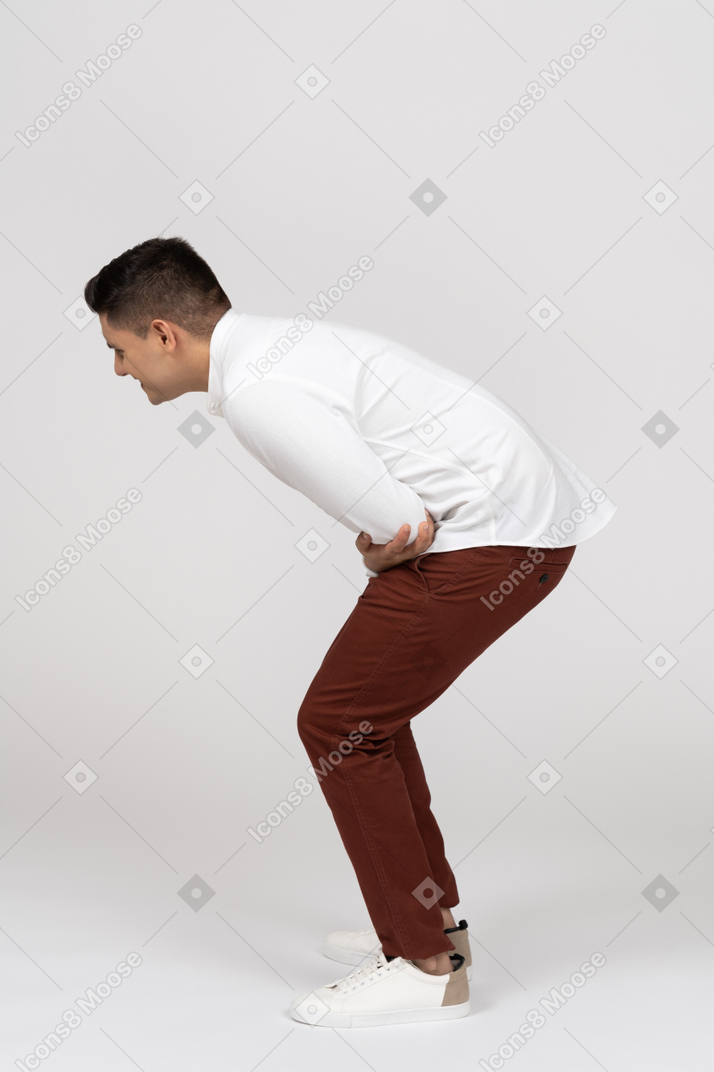 Vista lateral de un joven latino en cuclillas y riendo a carcajadas