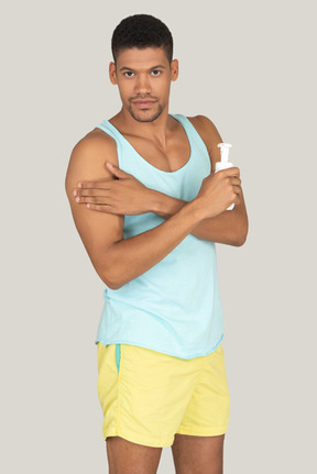 Man in blue tank top and yellow shorts applying suncream